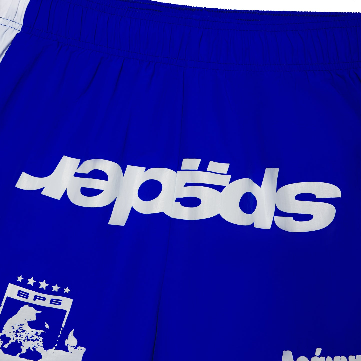 Blue 4oz water repellent nylon soccer shorts with white graphic print, wide side stripe, and elastic waistband.