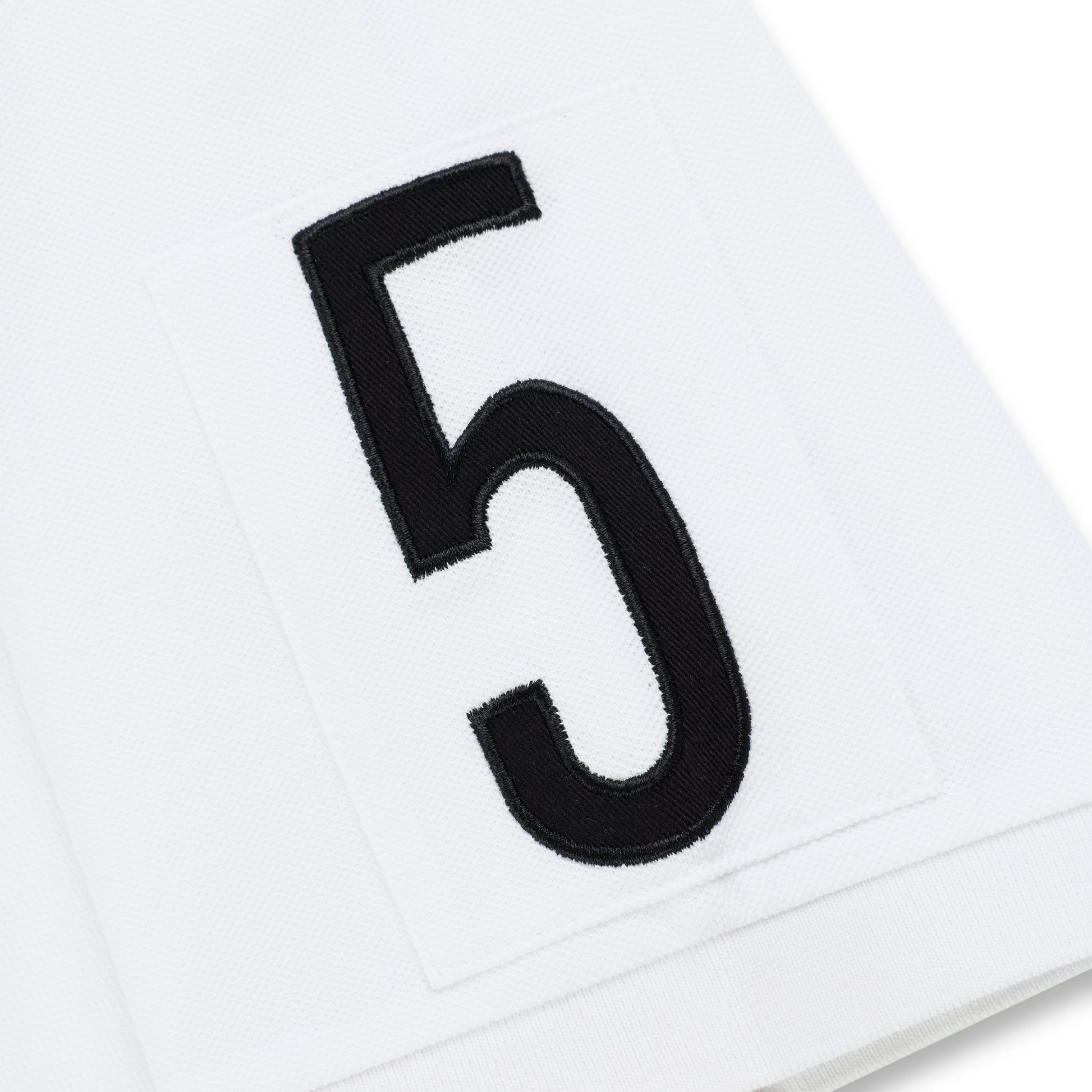 White polo shirt with an embroidered black number 5 patch.