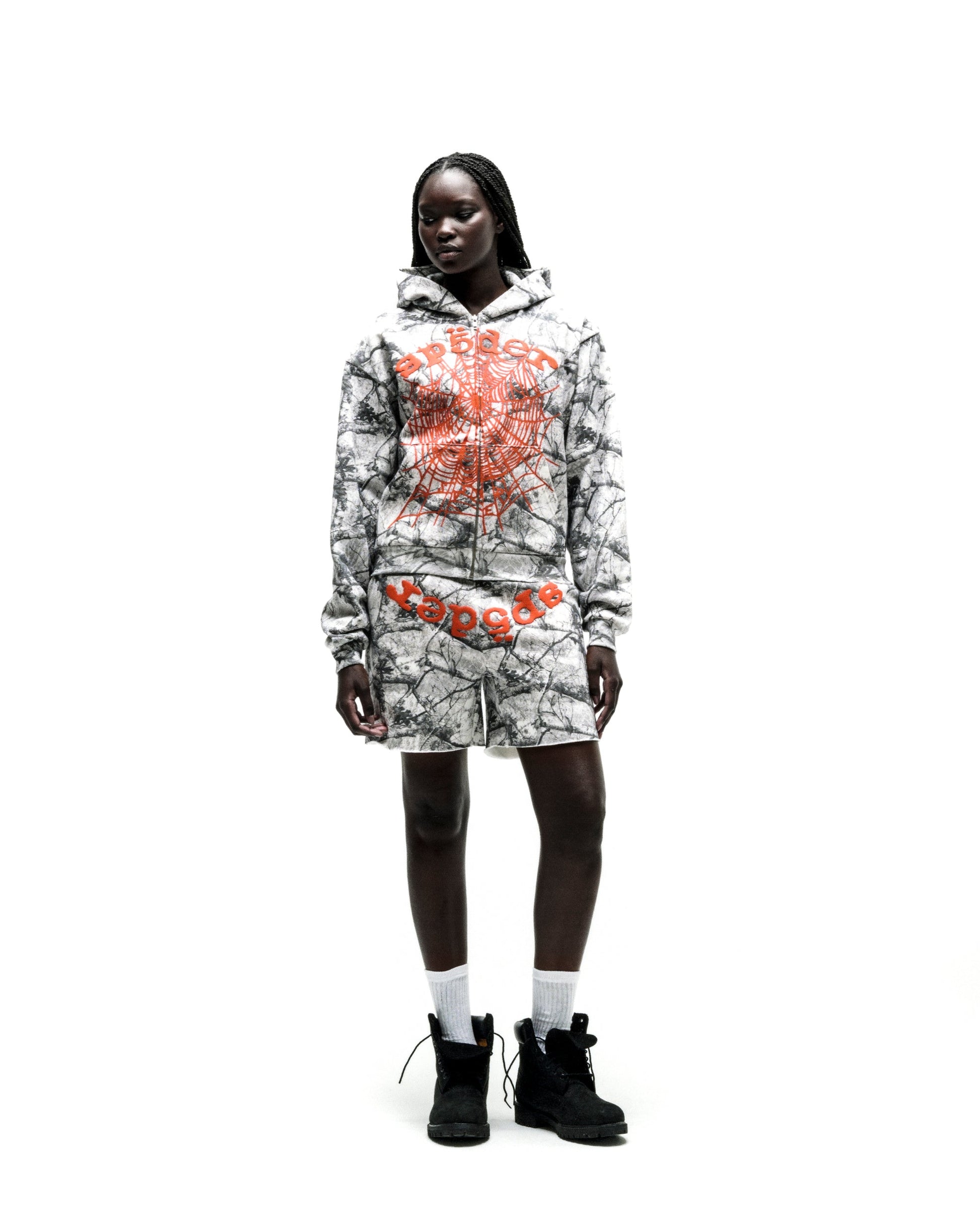 Model wearing a REALTREE OG WEB V2 ZIP HOODIE and matching shorts with orange puff print spiderweb design.