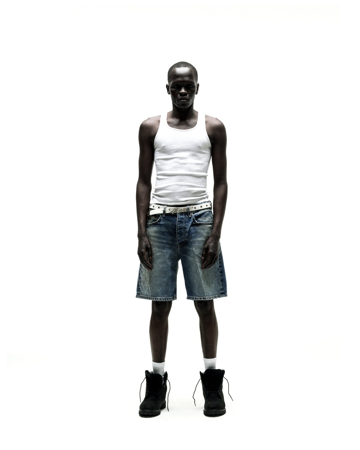 Man wearing vintage wash denim shorts with rhinestone web design, a white tank top, and black boots.