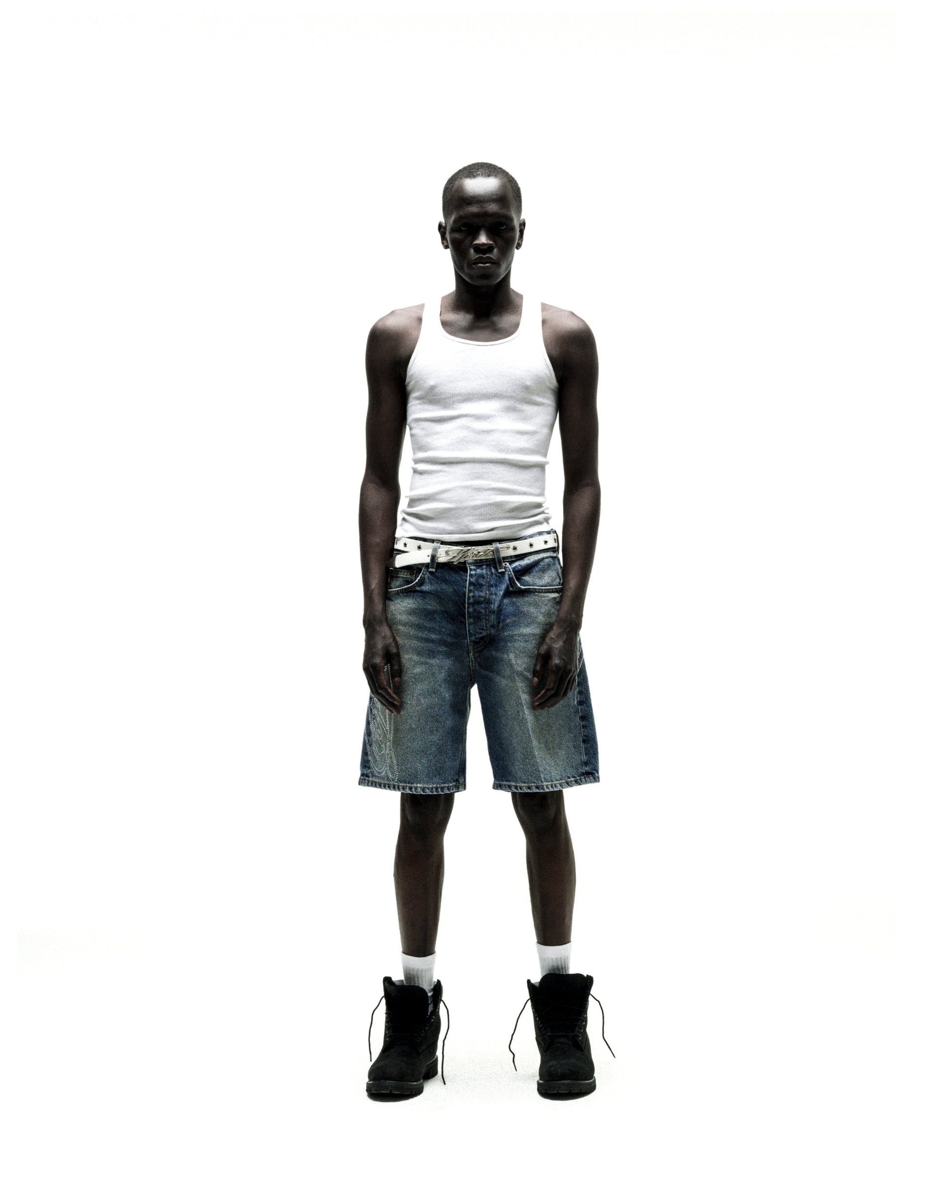 Man wearing vintage wash denim shorts with rhinestone web design, a white tank top, and black boots.