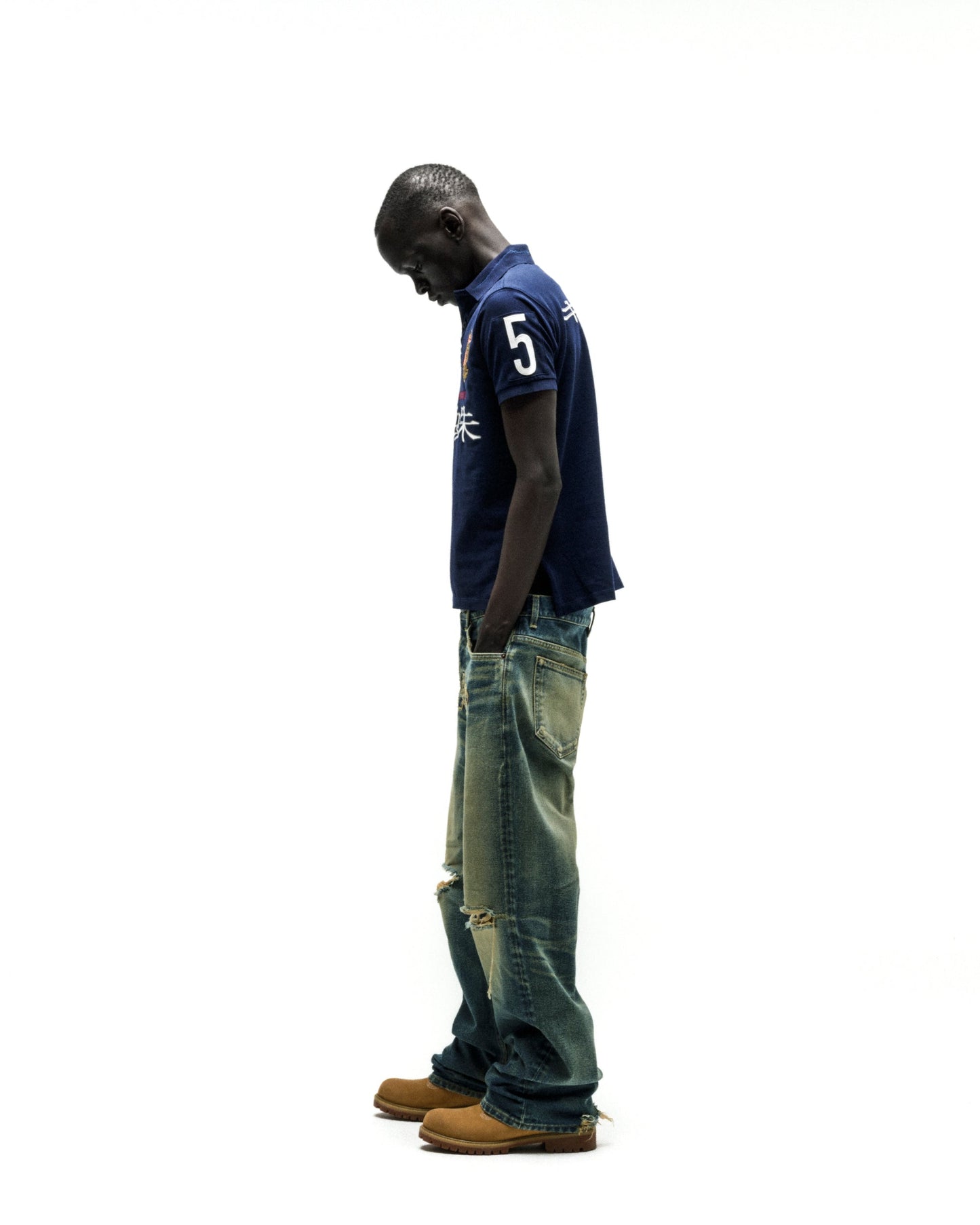 Dark blue polo shirt with "5" and Japanese text, paired with distressed wide-leg jeans and tan boots.