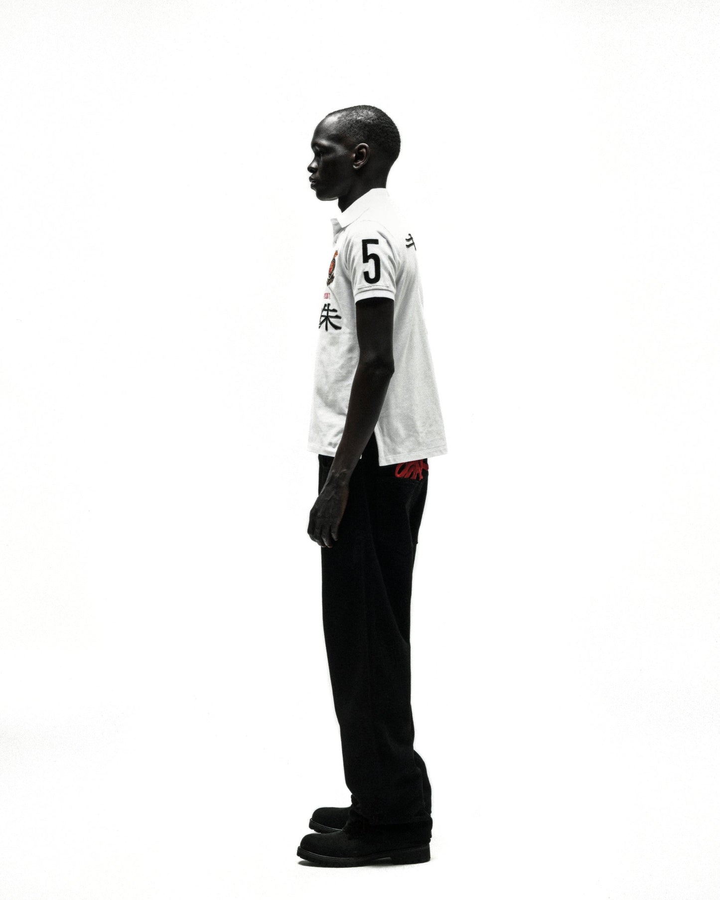 White polo shirt with "5" and red Japanese characters, black pants, and shoes on a male model.