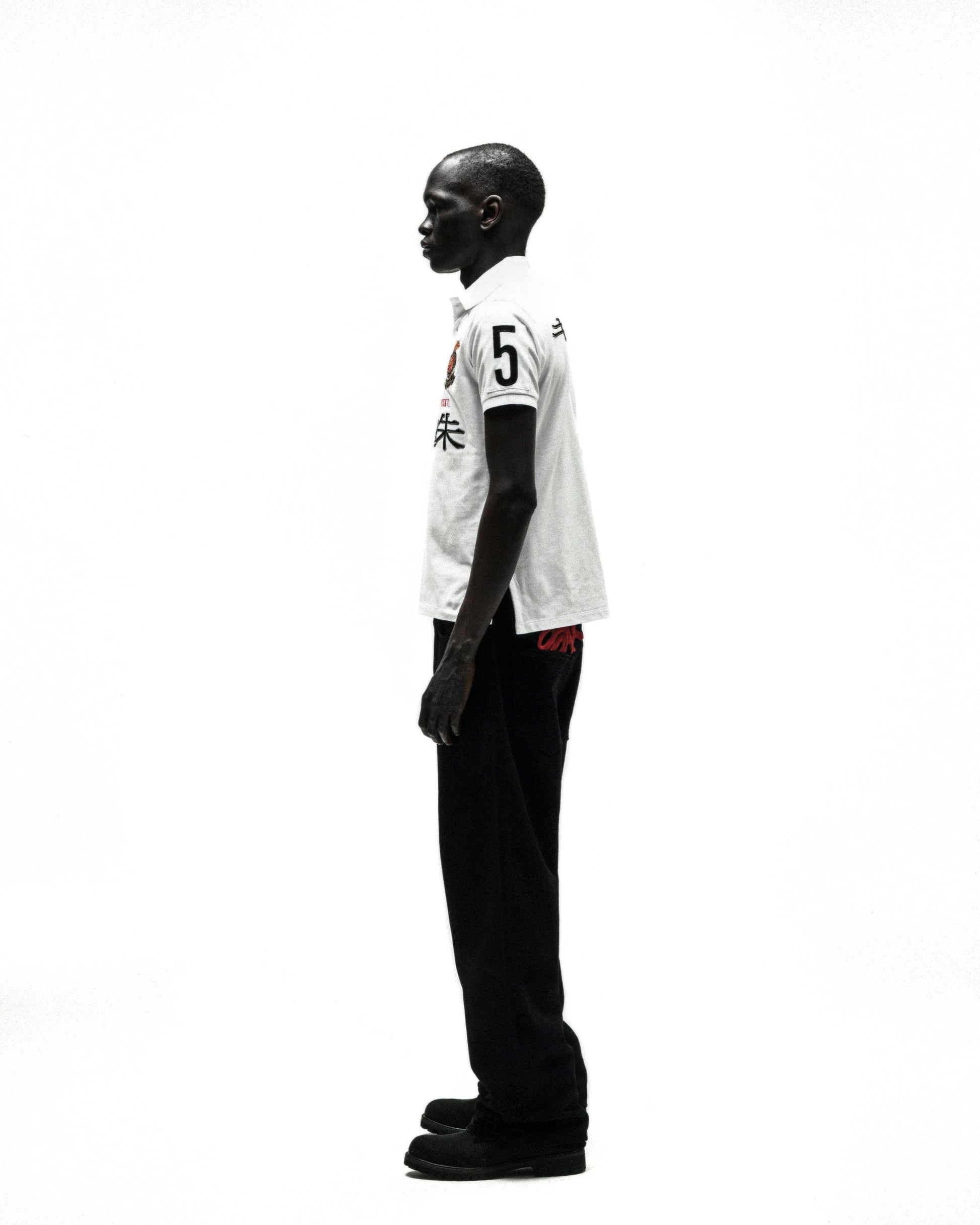White polo shirt with "5" and red Japanese characters, black pants, and shoes on a male model.