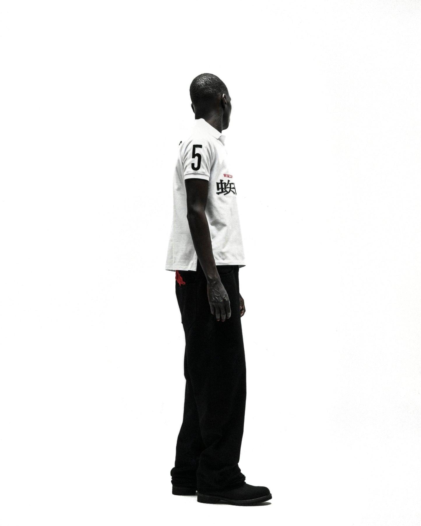 Man in white WORLDWIDE POLO shirt with "5" and Japanese text, black pants, and shoes, side view.