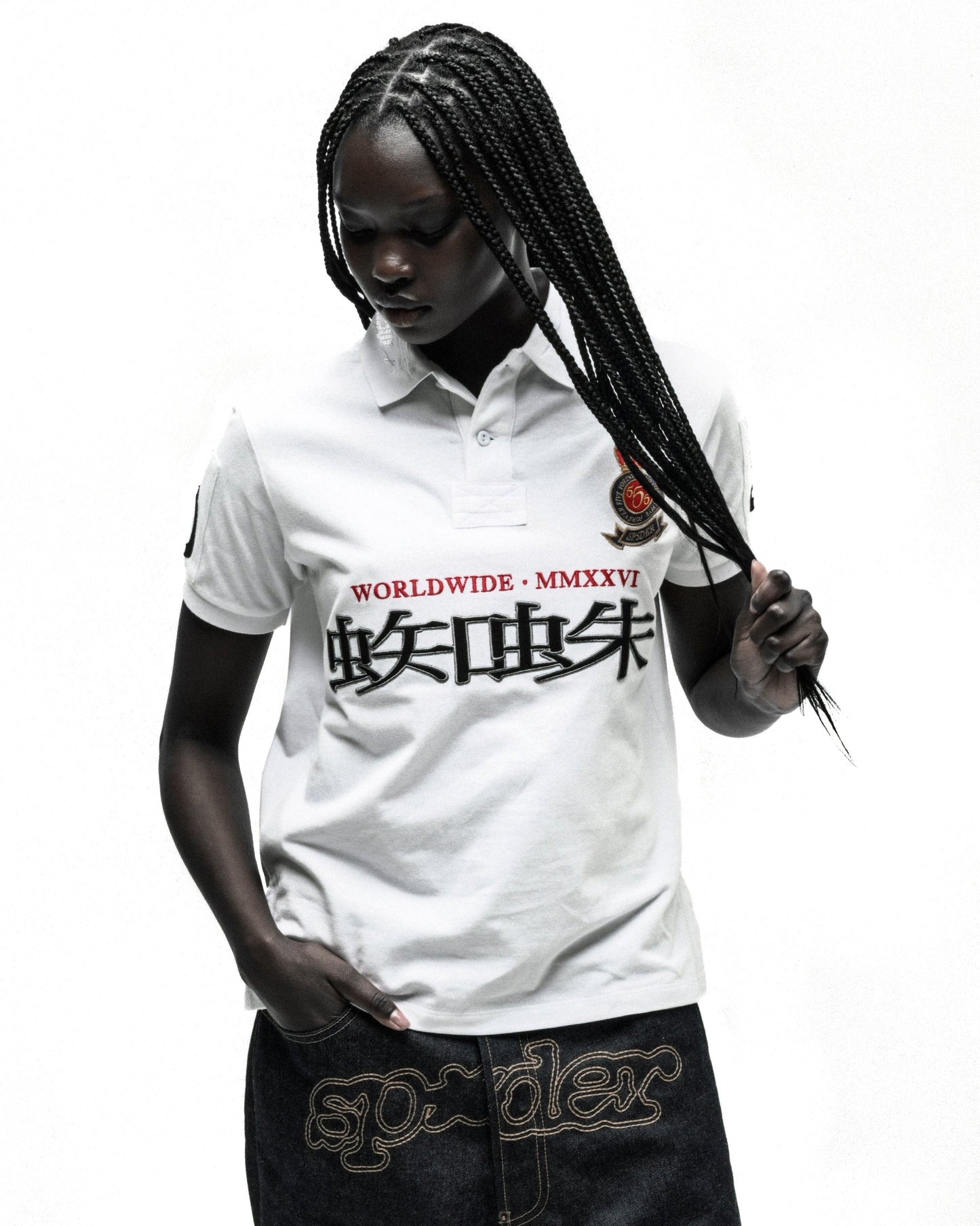 Woman in white "WORLDWIDE MMXXVI" polo shirt with black Japanese text and embroidered crest, dark denim shorts.
