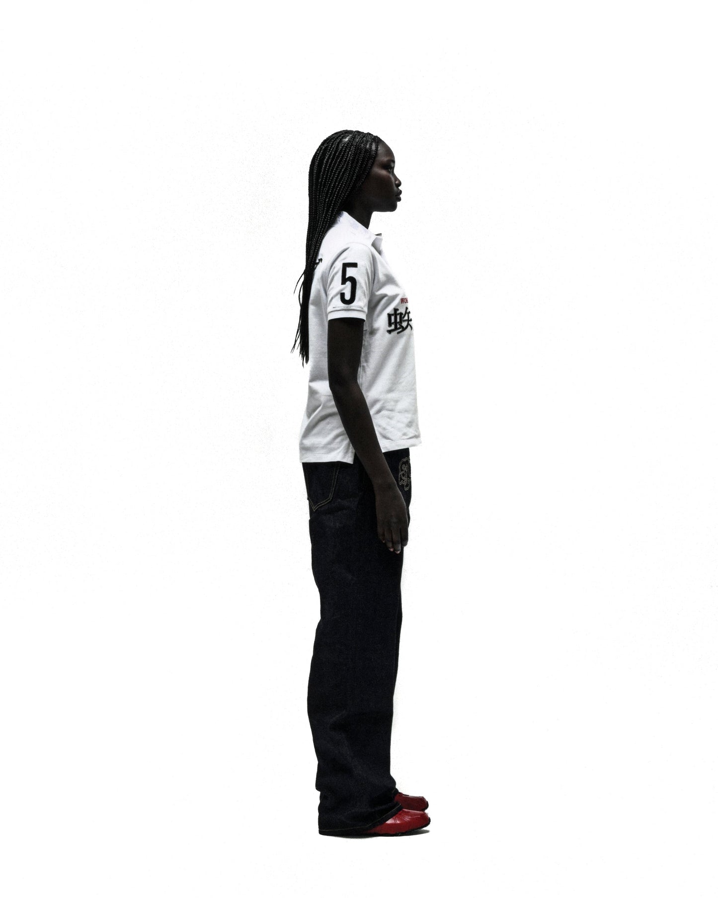 Woman in white WORLDWIDE POLO shirt with "5" and black text, dark jeans, and red shoes.
