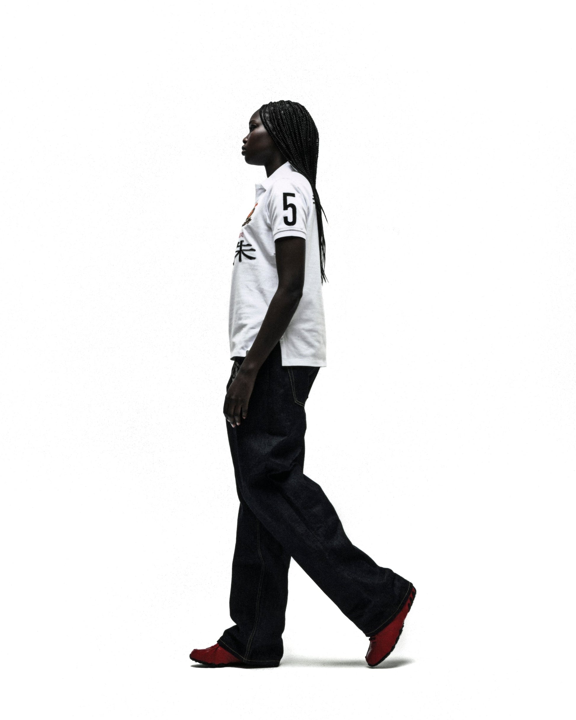 Worldwide Polo white short-sleeve shirt with "5" and red/orange embroidery, paired with dark jeans and red shoes.