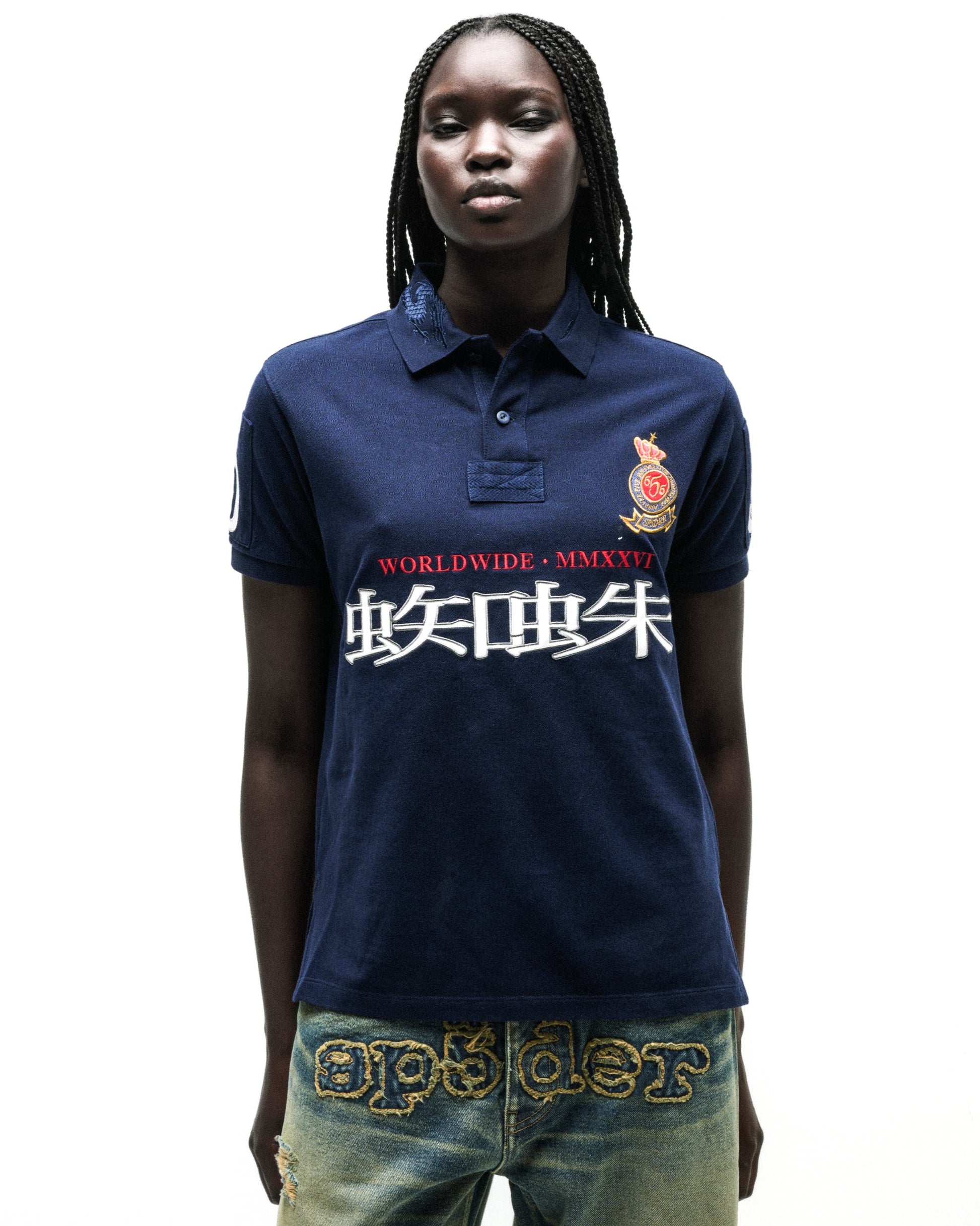 Navy blue polo shirt with "WORLDWIDE • MMXXVI" and white Japanese characters, red crest, and distressed denim.