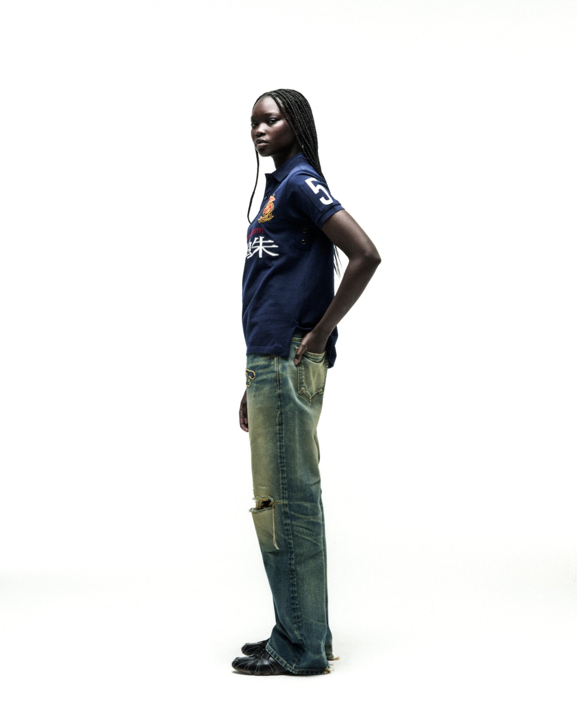Dark-skinned model in a navy blue WORLDWIDE POLO shirt with white numbers and red text, paired with distressed jeans.