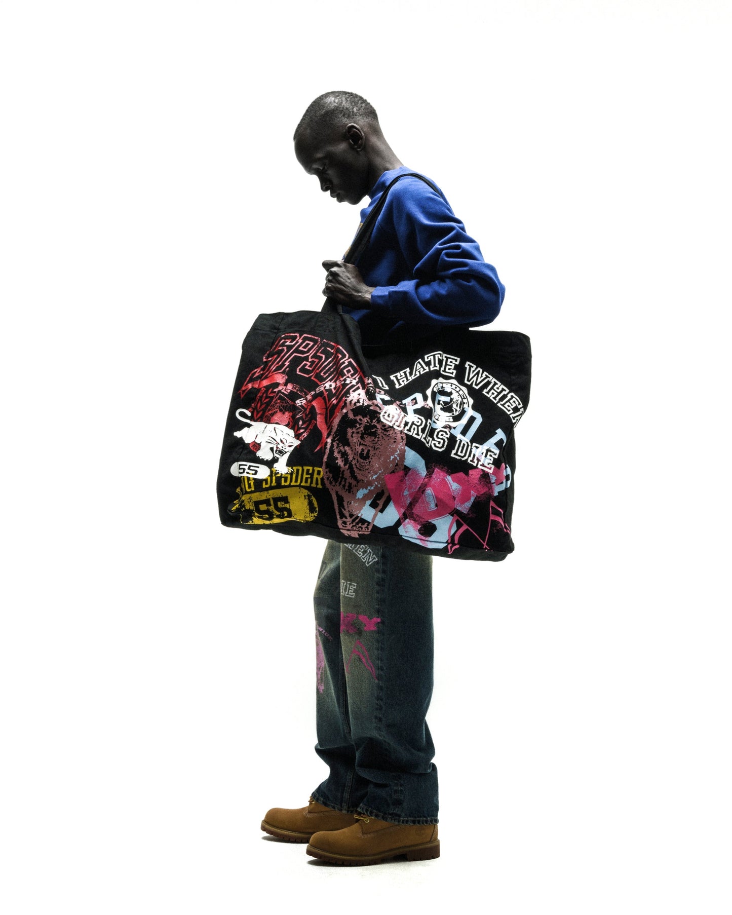Man holding a black brushed twill tote bag with colorful graphic prints on both sides.