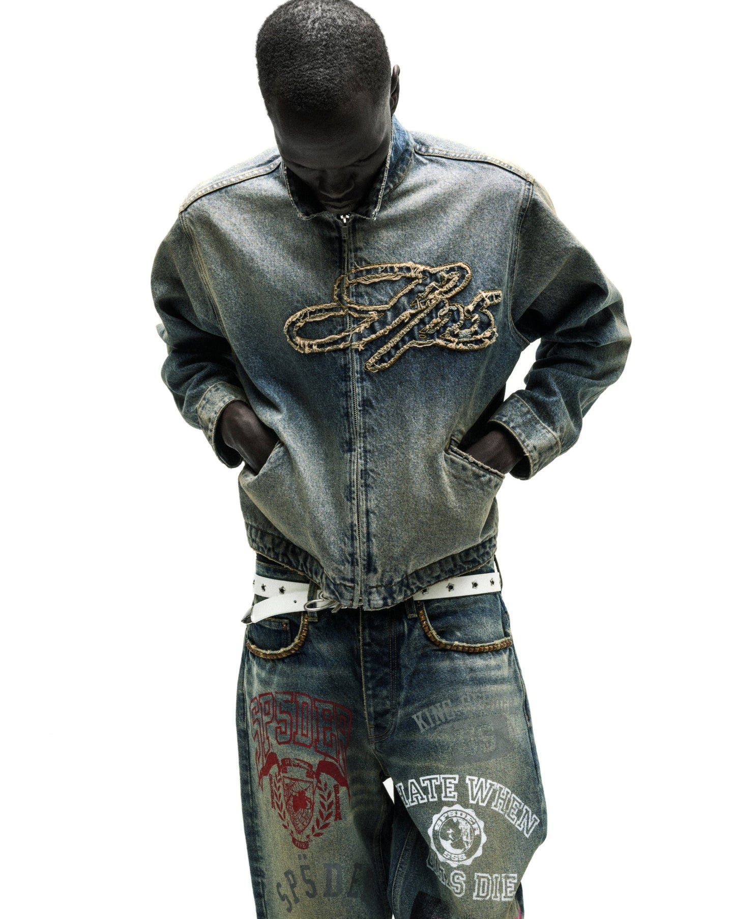 Washed blue denim work jacket with embroidered script logo, worn with matching jeans and white belt.