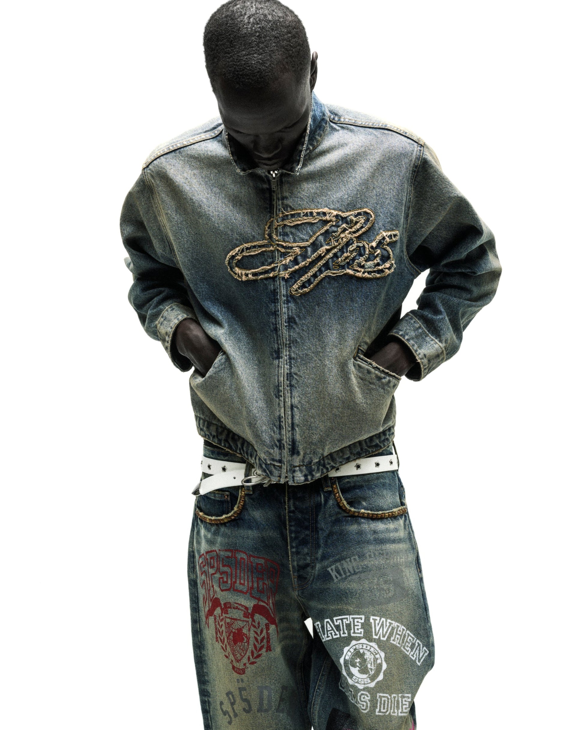 Washed blue denim work jacket with embroidered script logo, worn with matching jeans and white belt.