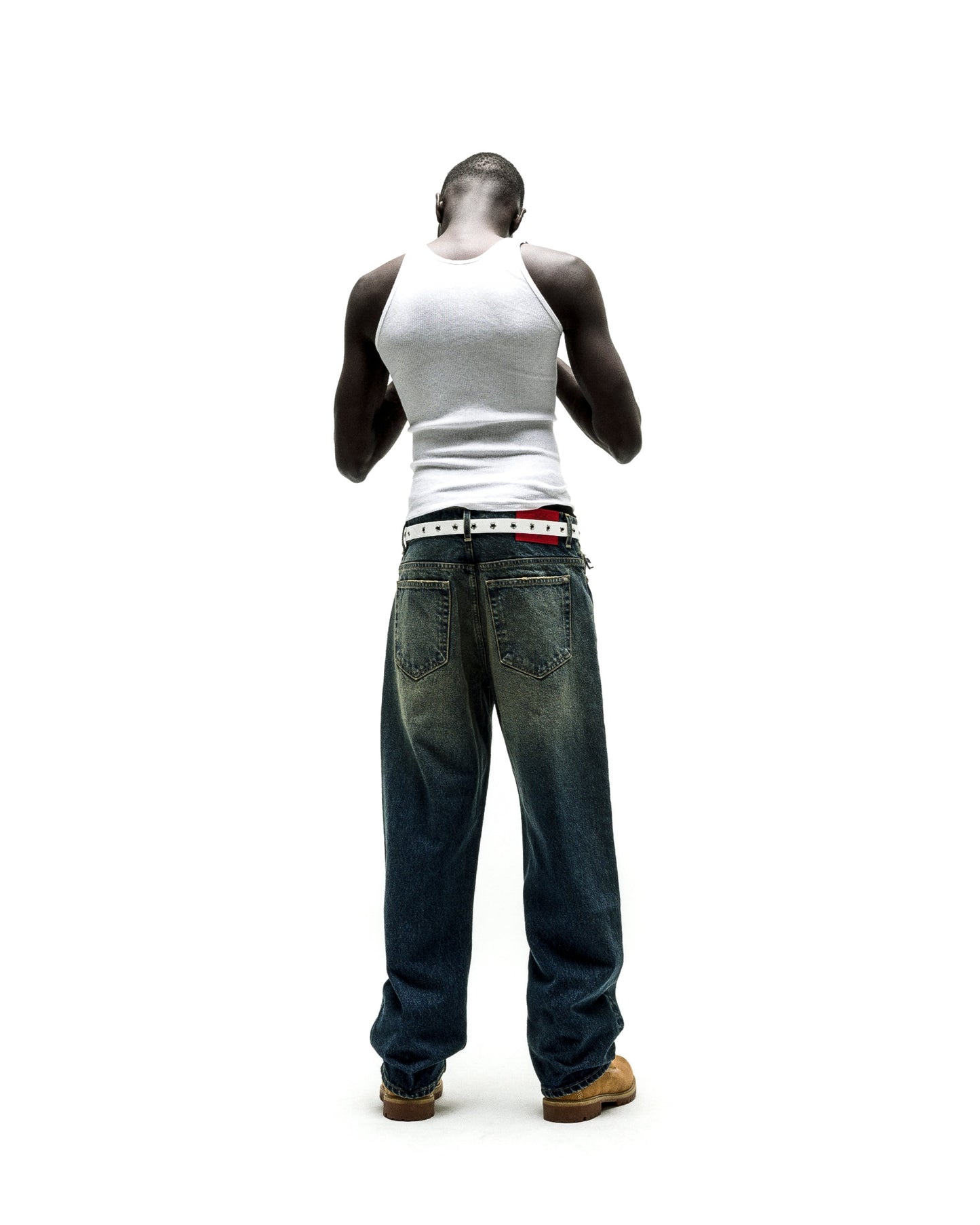 Man from behind wearing baggy, dark wash BIG PRINT JEANS with a white belt and tank top.