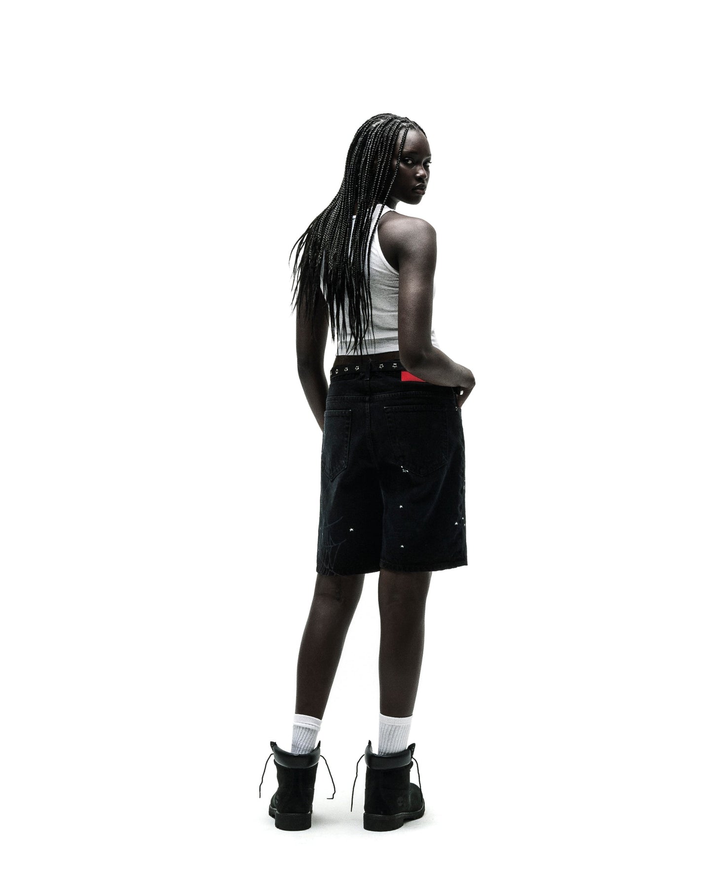 Woman in black HEAVY WEB JEAN SHORTS with white paint splatters, a white tank top, and black boots.