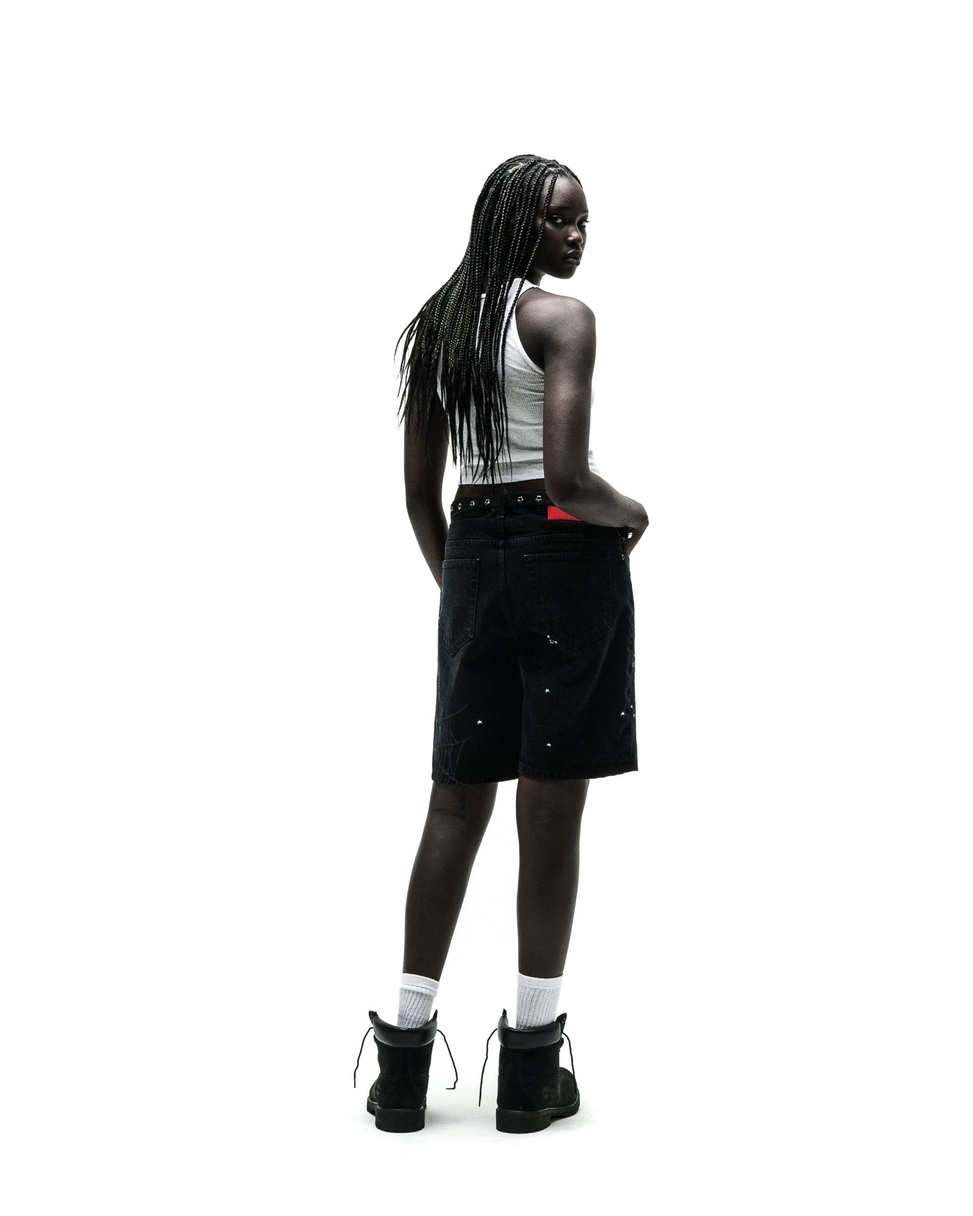 Woman in black HEAVY WEB JEAN SHORTS with white paint splatters, a white tank top, and black boots.