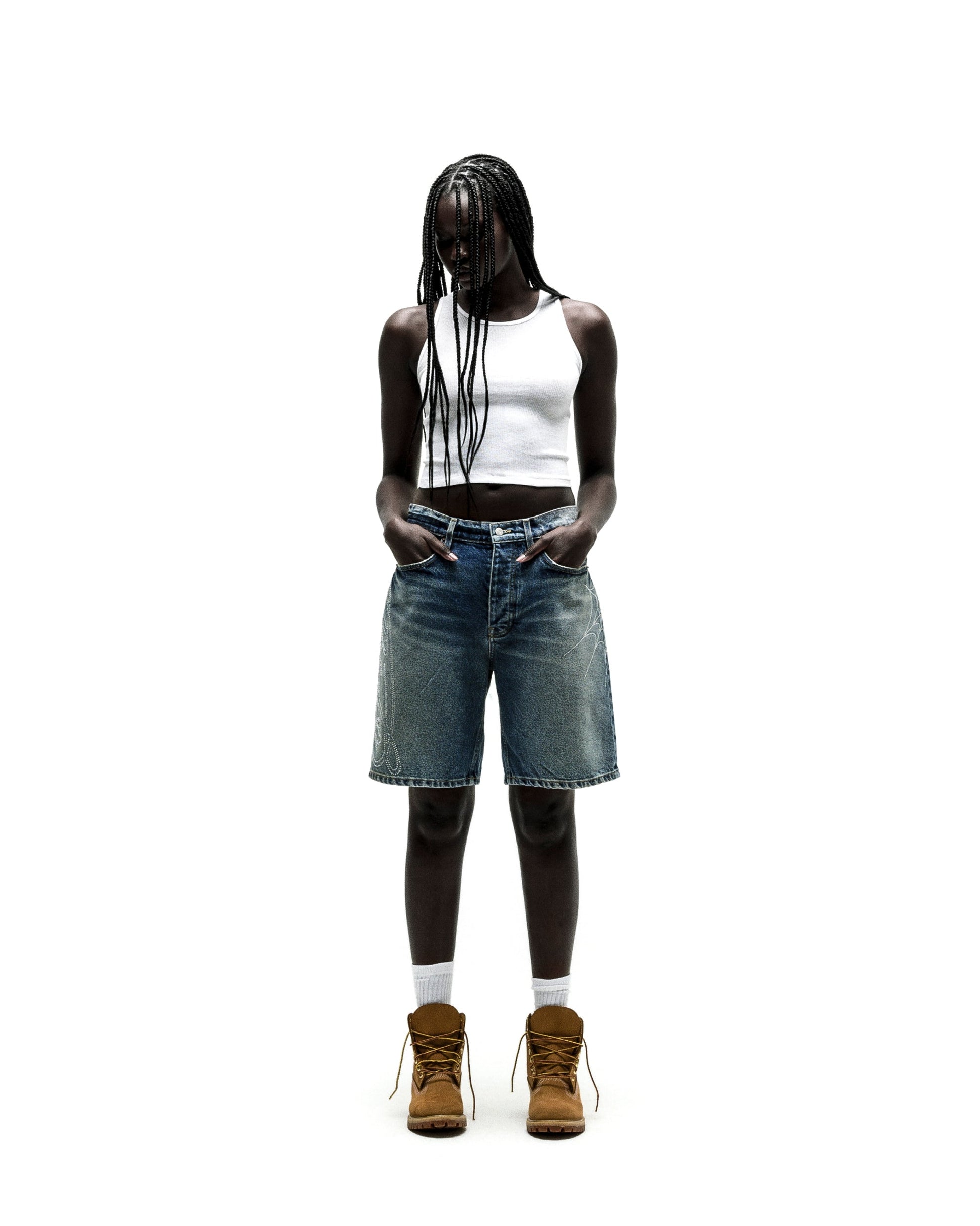 Model in vintage wash denim shorts with rhinestone web design, white tank top, and brown boots.