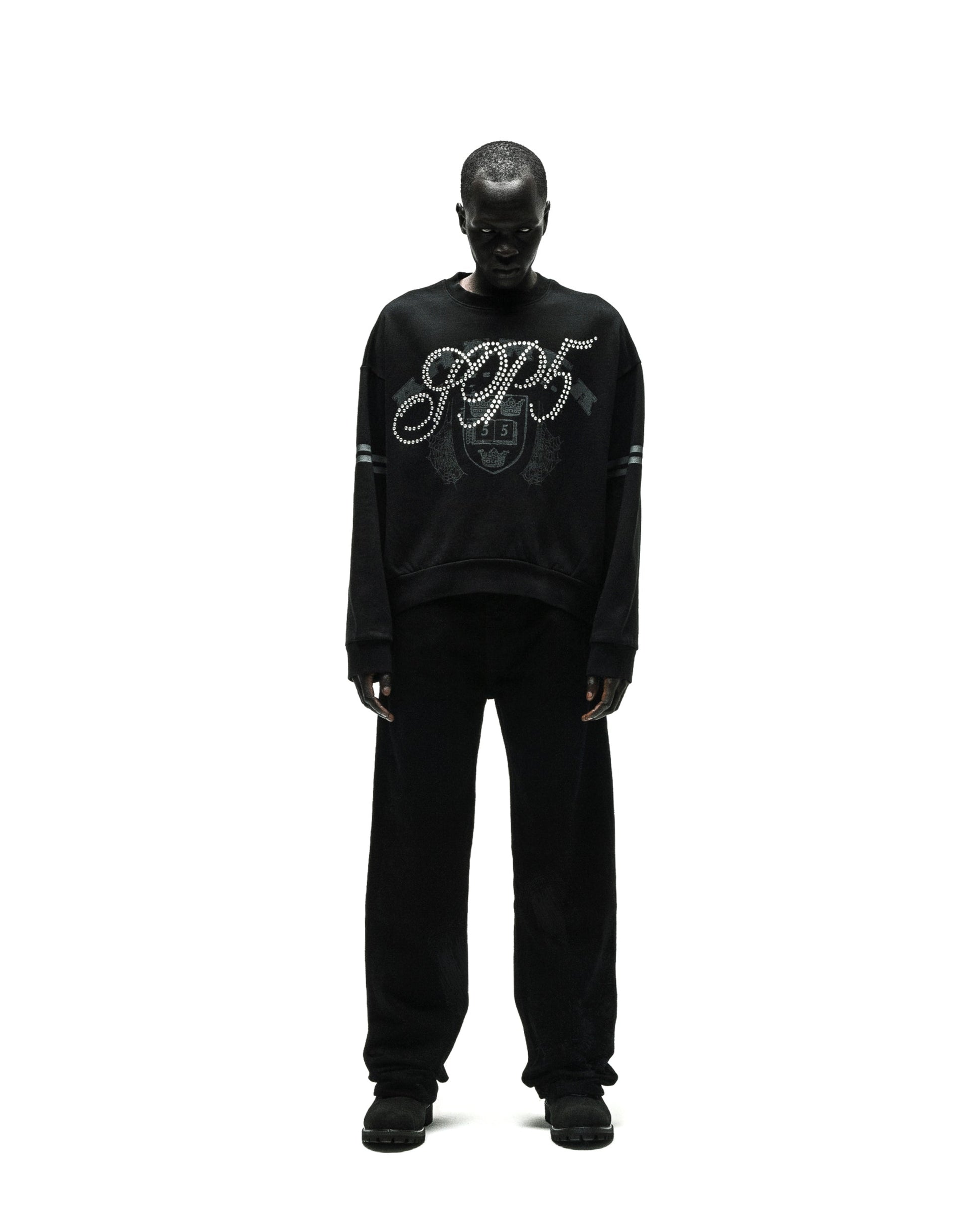 Black ARANEA CREWNECK with "SP5" rhinestone logo and striped sleeves, worn by a model.