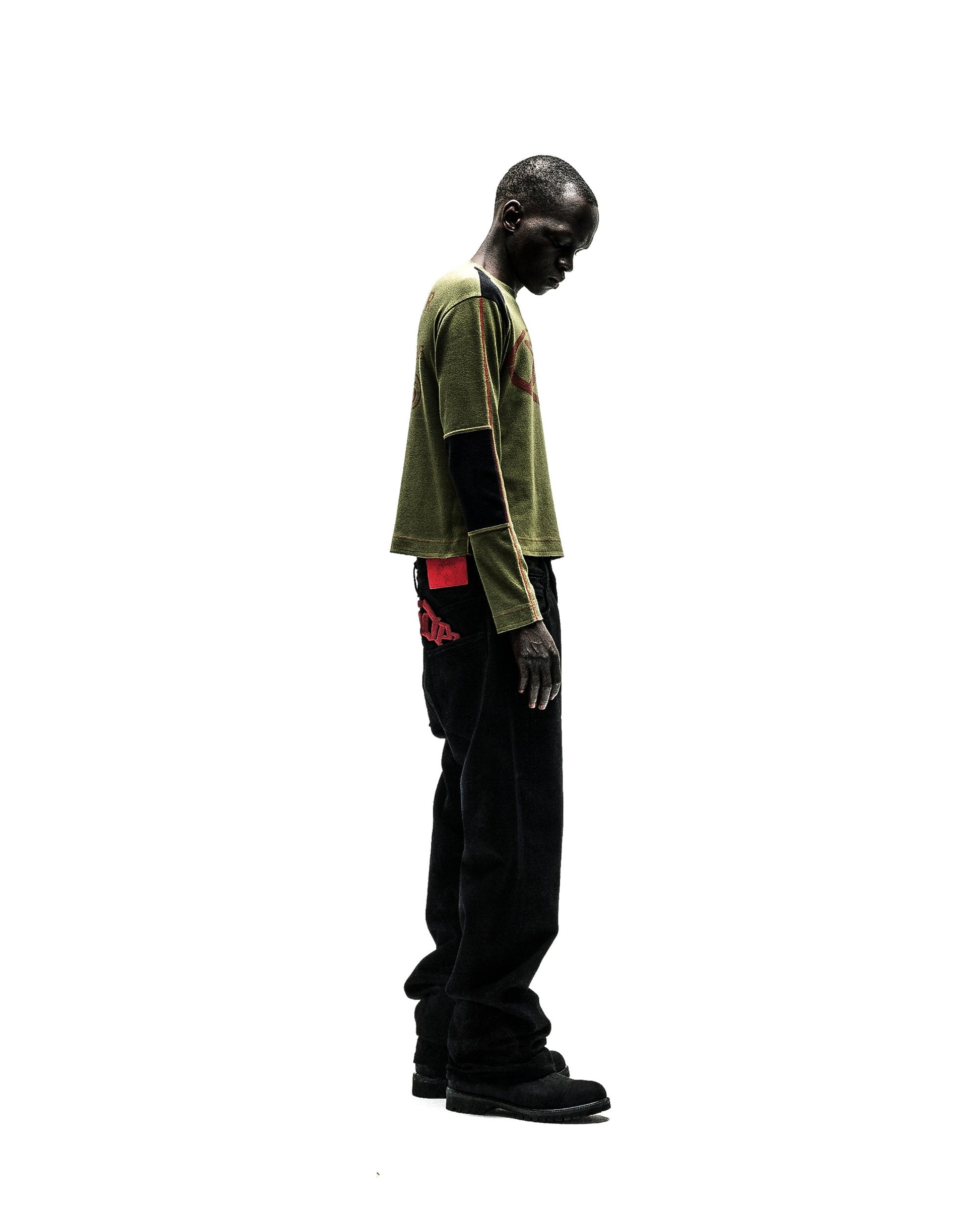 Man wearing an olive green SERVICE LONGSLEEVE with red graphic, black sleeves, and black jeans.