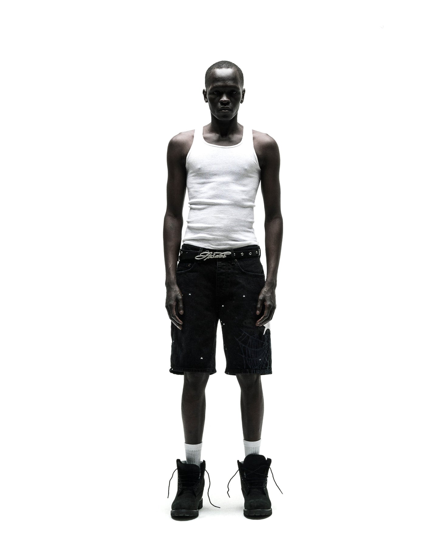Man in black HEAVY WEB JEAN SHORTS with white web graphic, white tank top, and black boots.