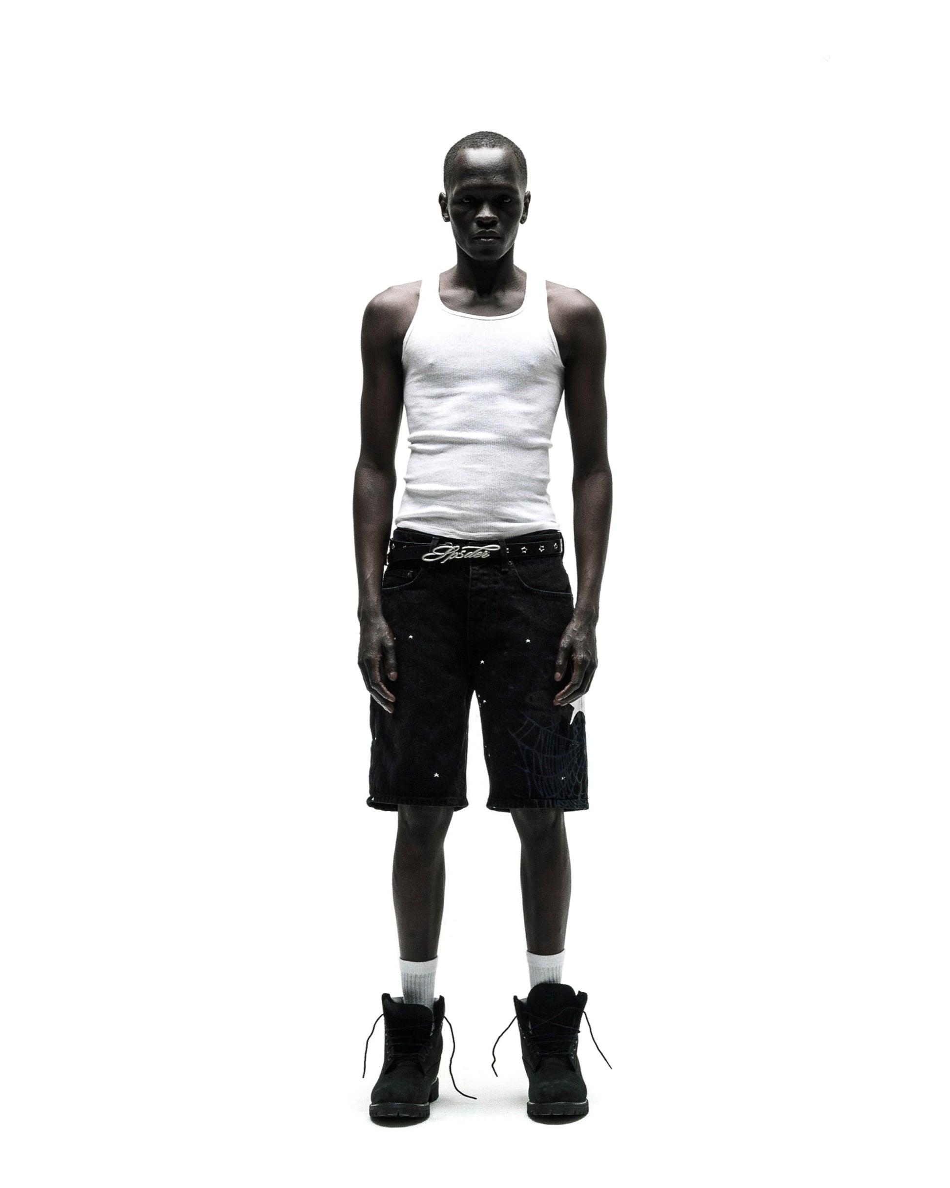Man in black HEAVY WEB JEAN SHORTS with white web graphic, white tank top, and black boots.
